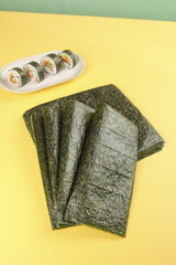 Dried nori seaweed sheets with sushi rolls on yellow background © LyVan