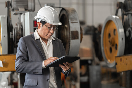 Senior Asian man in hard hat and suit standing in industrial factory