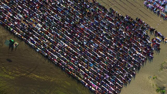 Cinematic high aerial drone shot of thousands of Muslim worshippers performing synchronized Sholat Idul Fitri prayer on sandy gumuk pasir in Yogyakarta.