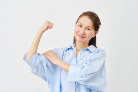 白背景で力こぶのポーズをする高齢女性