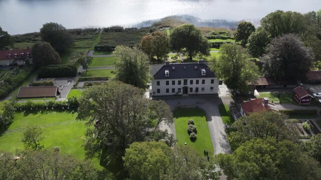 Aerial drone view of Rada Sateri historic manor estate with formal gardens and tree lined grounds. White manor house sits among landscaped parkland, pathways and surrounding woodland
