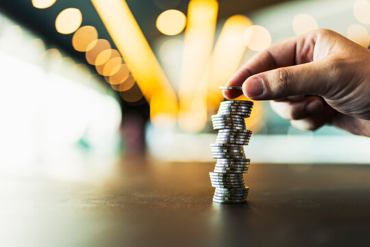 Hand placing coin on top of money stack. Financial investment, savings growth, wealth accumulation, banking, and profit concept for business.