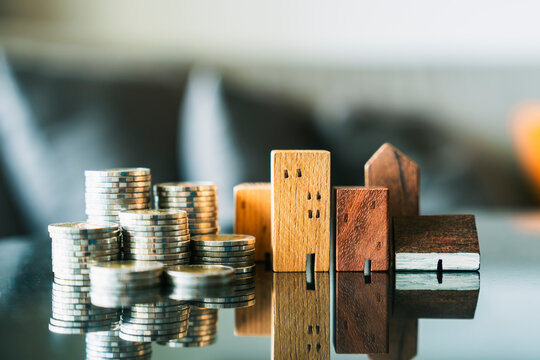 Real estate wooden house models with coins stacks. Property investment, home loan capital, residential market valuation concept.