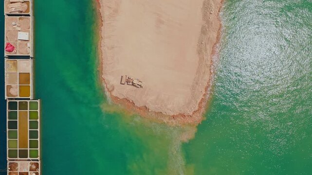 Top-down aerial view of a bulldozer moving sand and earth into the vibrant turquoise water, creating a new artificial land peninsula next to salt evaporation ponds