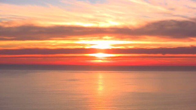 雲のある水平線の夕日と赤く染まった海岸線から海面