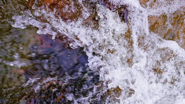 Overhead shot of clear stream flowing through colorful rock texture