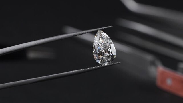 Exquisite pear-shaped diamond with swaying slightly with sparkles brilliantly in tweezers, showcasing rare luxury and investment value