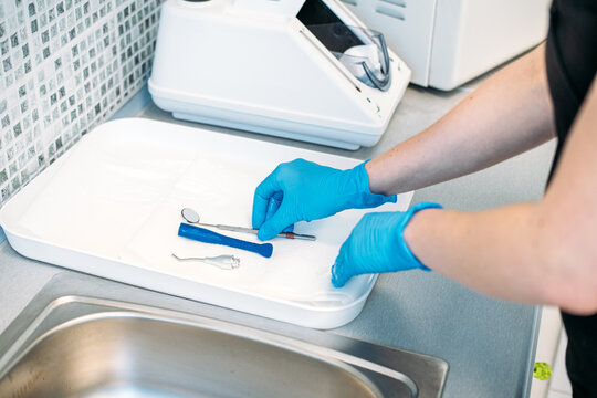 Gloved hands wipe small dental mirror with paper towel on tray before packaging. Dental tray preparation, arranging dental instruments, instrument drying tray.