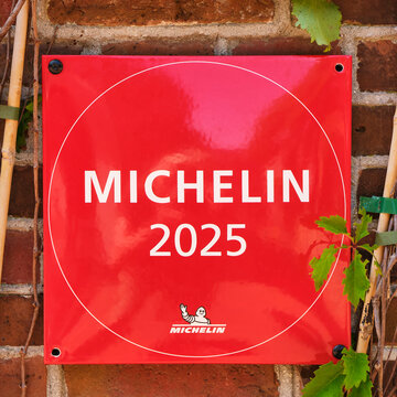 A close-up view of a bright red Michelin 2025 restaurant award sign with the iconic Michelin Man logo displayed on a textured brick wall.
