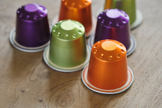 Closeup of colorful coffee capsules in green, orange and purple on a wooden table..	