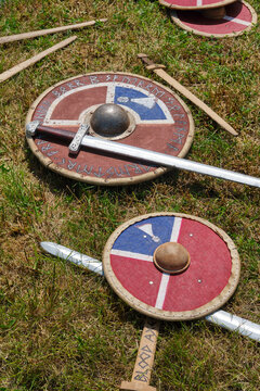 Authentic looking Viking age weaponry including round shields and long swords are displayed on a green grassy field for historical reenactment.
