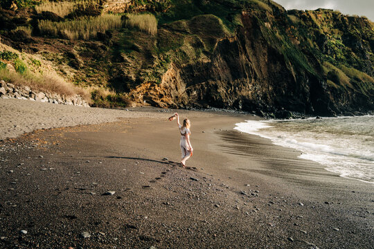 Woman walks barefoot on dark sand beach