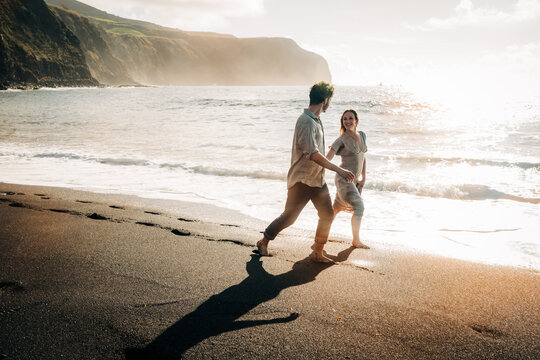 Happy couple walks along a black sand beach at sunset
