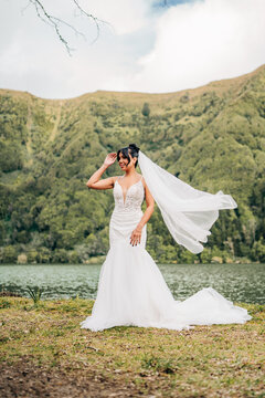 Beautiful bride with veil blowing by a mountain lake