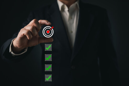 Businessman hand holding a virtual target dartboard and checklist with green checkmarks. Concept of business goal achievement, successful strategy, target planning, and task completion.