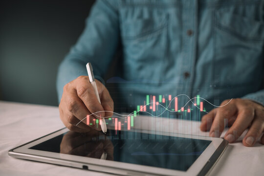 Businessman using a stylus pen on a digital tablet with glowing stock market candlestick charts. Concept of financial investment, trading, cryptocurrency analysis, and wealth management.