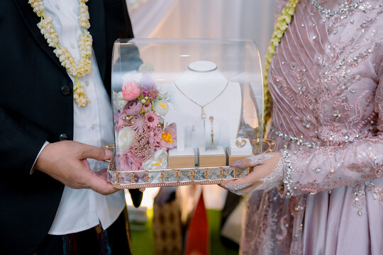 Bride and groom holding a decorated dowry tray with gold jewelry set during Indonesian wedding ceremony.