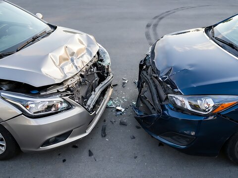 Two severely damaged cars with crumpled hoods after a headon collision on a road