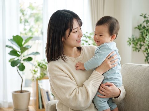 ソファの横で赤ちゃんを抱っこし満面の笑みで見つめ合う母親の女性
