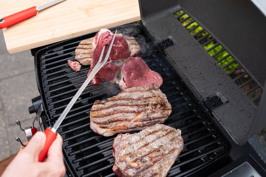 Grilling meat outdoors on barbecue grill with tongs