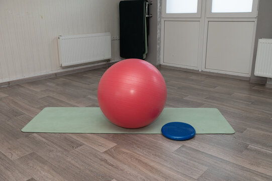 Empty fitness studio with red exercise ball on yoga mat and blue balance disc
