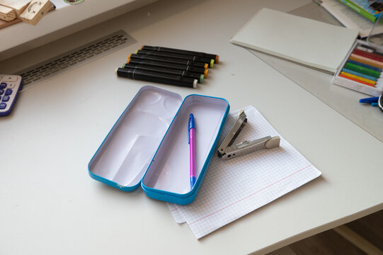 Desk with empty pencil case, pens, notebook, and stapler in study setting