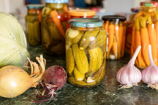Assorted pickled vegetables in jars with fresh onions and garlic on a rustic kitchen counter. National Pickle Day