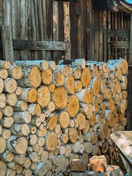 Stacked firewood logs against rustic wooden shed wall, countryside wood storage background.