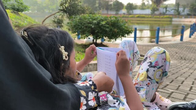 Close-up of Asian child solving multiplication math problems in notebook outdoors