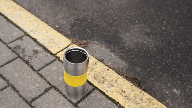 Stainless steel travel mug with yellow grip on sidewalk edge