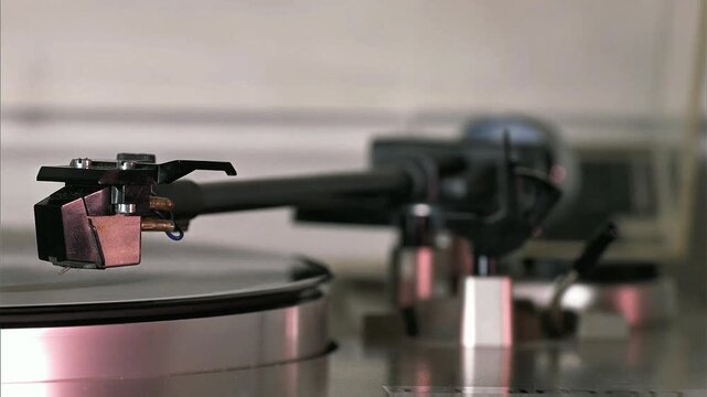 Close shot of turntable tonearm assembly resting gently on vinyl surface, metallic details with soft blurred background