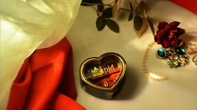 Golden-trimmed heart-shaped keepsake box with red rose, gemstone jewelry and pearl strand on soft warm fabric