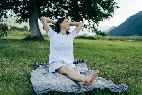 Happy peaceful girl relaxing under large tree, breathing fresh air with closed eyes. Freedom and mindfulness concept.