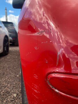 Nahaufnahme eines Kratzers und Lackschadens an einem roten Auto. Fahrzeugschaden, Parkrempler, Unfall, Versicherung, Kfz-Reparatur, Smart Repair und Karosserieschaden.