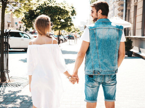 Smiling beautiful female and her handsome boyfriend posing in the street. Woman in casual summer dress and man in jeans clothes. Happy cheerful couple family having fun in sunglasses.Shows peace sign