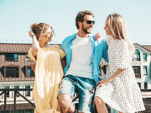 Group of young three stylish friends posing in the street. Fashion man and two cute female dressed in casual summer clothes. Smiling models having fun in sunglasses.Cheerful women and guy outdoors