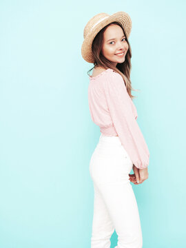 Young beautiful smiling female in trendy summer clothes. carefree woman posing near blue wall in studio. Positive brunette model having fun. Cheerful and happy. In hat