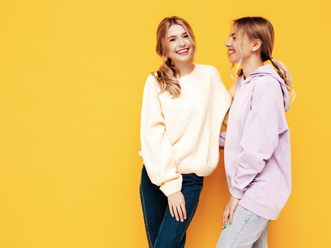 Two young beautiful smiling blond hipster female in trendy summer clothes. Sexy carefree women posing near yellow wall in studio. Positive models having fun. Cheerful and happy