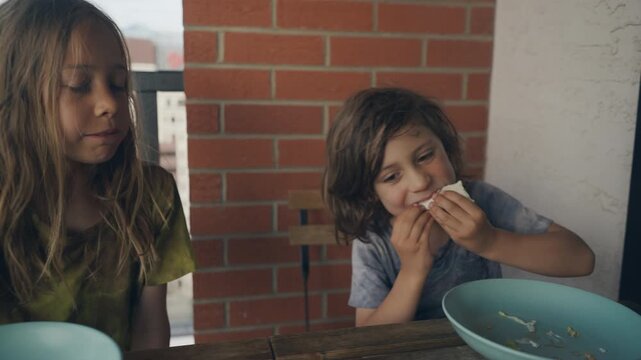 Two siblings sharing a meal of fresh wraps on a balcony