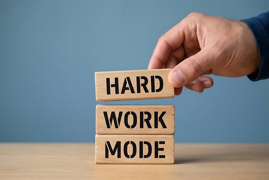 Hand stacking wooden blocks spelling 'HARD WORK MODE' on a table, symbolizing dedication and productivity. Business and Teamwork concept.