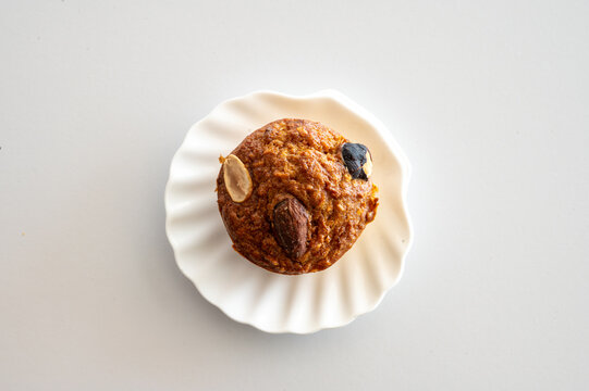 A close top view of a golden homemade muffin with almond and blueberry on a white plate a tasty and healthy snack on a light table.