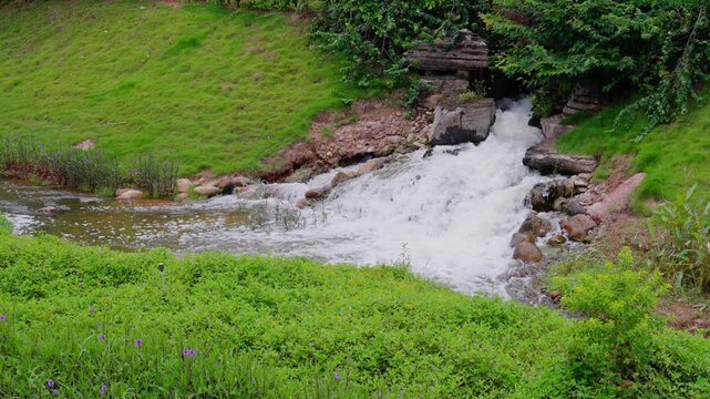 Garden waterfall and stream landscape surrounded by green grass slopes