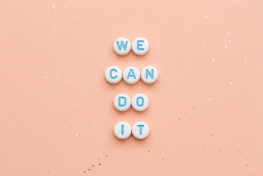 Beads spelling "We Can Do It" on pink background, motivational and achievement concept