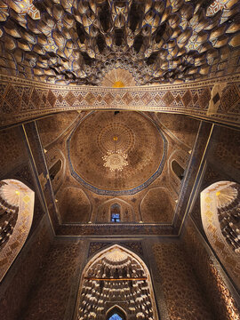 Ornate interior dome of Gur-e-Amir mausoleum in Samarkand featuring intricate muqarnas and golden patterns. Ideal for travel publications, cultural heritage articles, and architectural design.