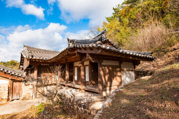 Fototapeta premium Scenic Exterior View of Traditional Korean Hanok Architecture Featuring Tiled Roofs, Earthen Wall, and Vibrant Autumn Foliage Under Blue Sky