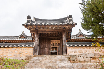 Fototapeta premium Symmetric Exterior View of Traditional Korean Hanok Entrance Gate Featuring Stone Stairs, Wooden Doors, and Tiled Roof