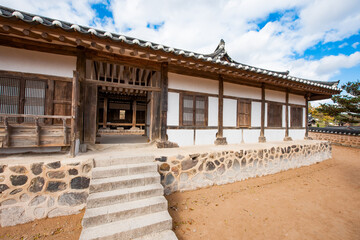 Obraz premium Exterior Perspective of Traditional Korean Hanok Building Featuring Stone Foundation, Wooden Structure, and Tiled Roof Under Sky with Clouds
