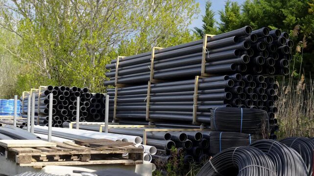 PVC pipes and industrial plastic conduits stacked in a storage yard. Construction supplies for infrastructure, drainage, and irrigation projects, neatly organized for transport and installation.