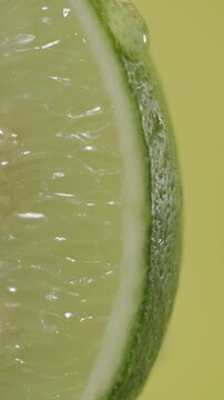 Macro shot of jeruk nipis (lime) with dripping glycerin on a light green background.
