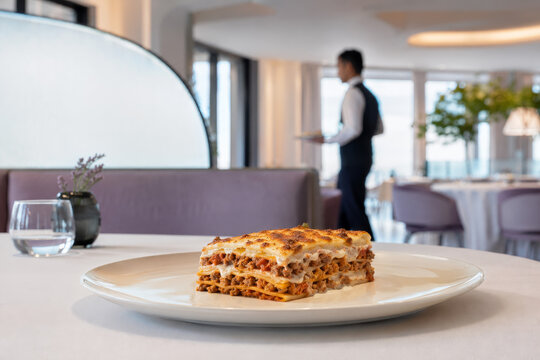 Un plato de lasa&ntilde;a servido en un restaurante elegante con un camarero en el fondo
